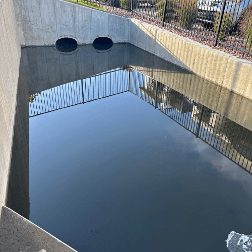 A clean detention pond with clear water reflecting the surrounding fence and environment.