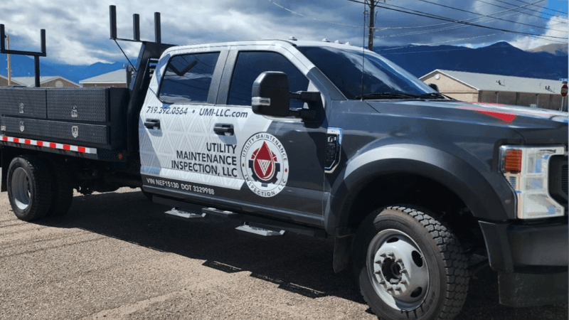 A utility maintenance inspection truck parked outdoors with a mountainous background, featuring the company's logo and contact information on the side.